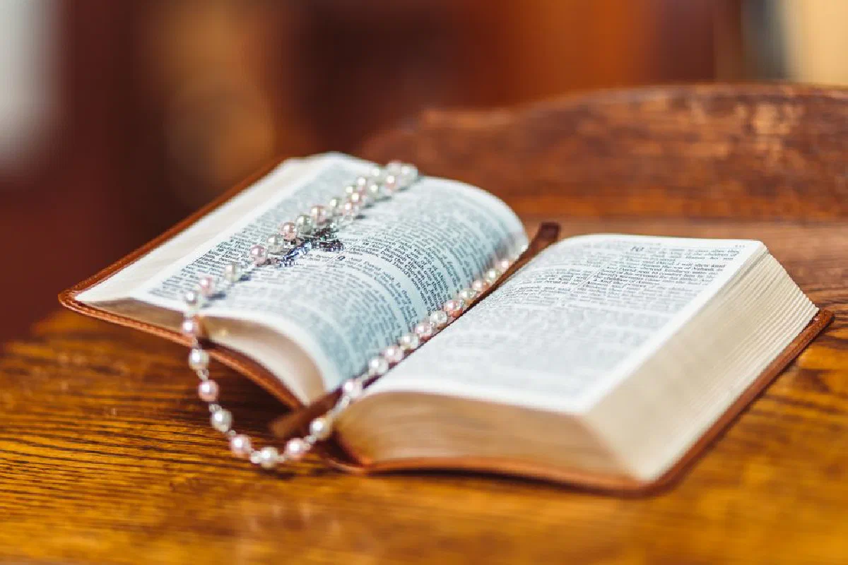 An open Bible with a detailed rosary lying on its pages resting on a wooden surface.