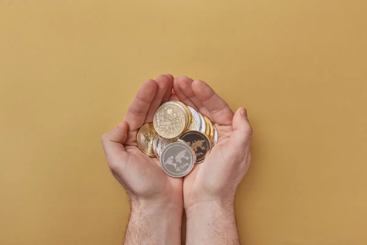 Close-up of hands holding various cryptocurrency coins over a yellow background, highlighting modern digital finance.