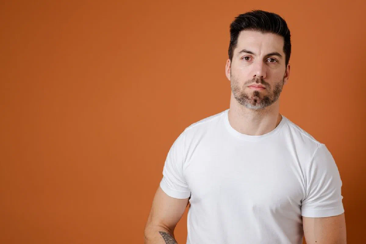 Portrait of a man wearing a white t-shirt standing against a solid orange background.