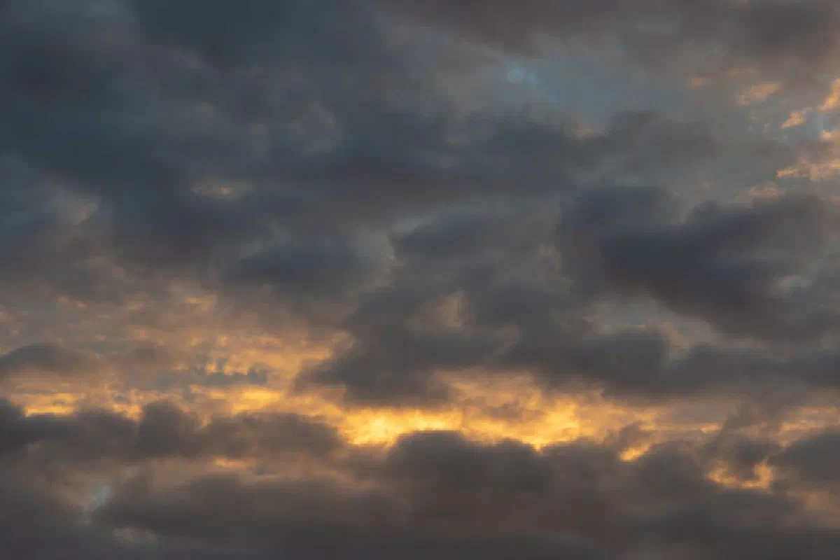 A dramatic cloudy sky with sun peeking through at sunrise, showcasing nature's beauty.