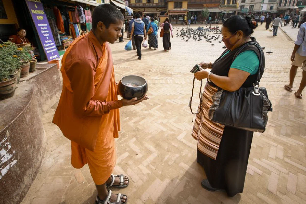 A Buddhist monk receives alms from a woman on a busy urban street, showcasing cultural traditions.