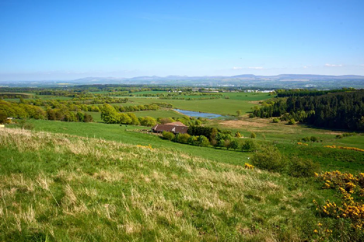 Breathtaking view of the Scottish countryside featuring rolling hills, farmlands, and a tranquil river under a blue sky.