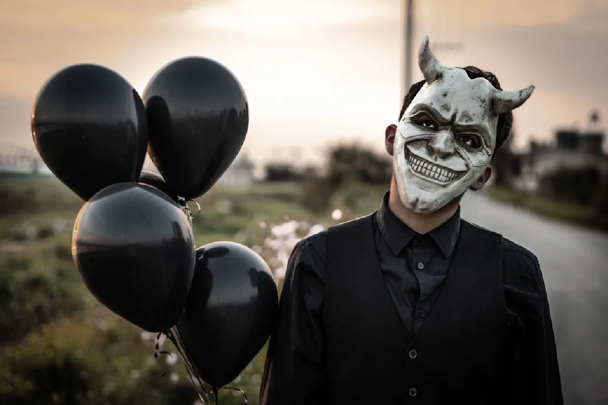 A spooky portrait featuring a masked figure with black balloons outdoors. Ideal for Halloween themes.
