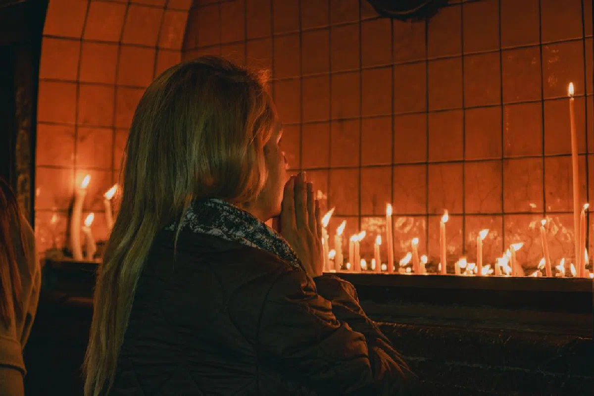 A woman prays beside lit candles in a dimly lit church, evoking a sense of peace and reflection.