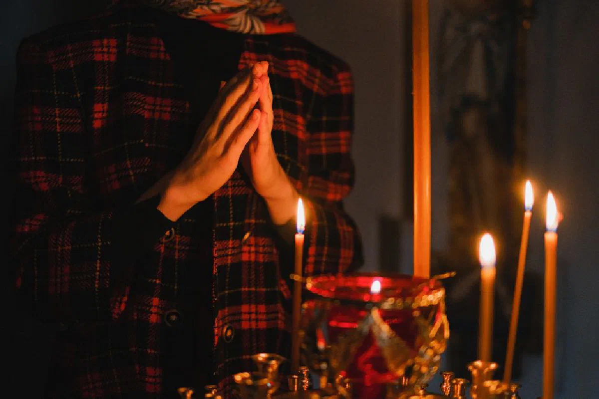 A person praying with candles in a dark, spiritual church setting.