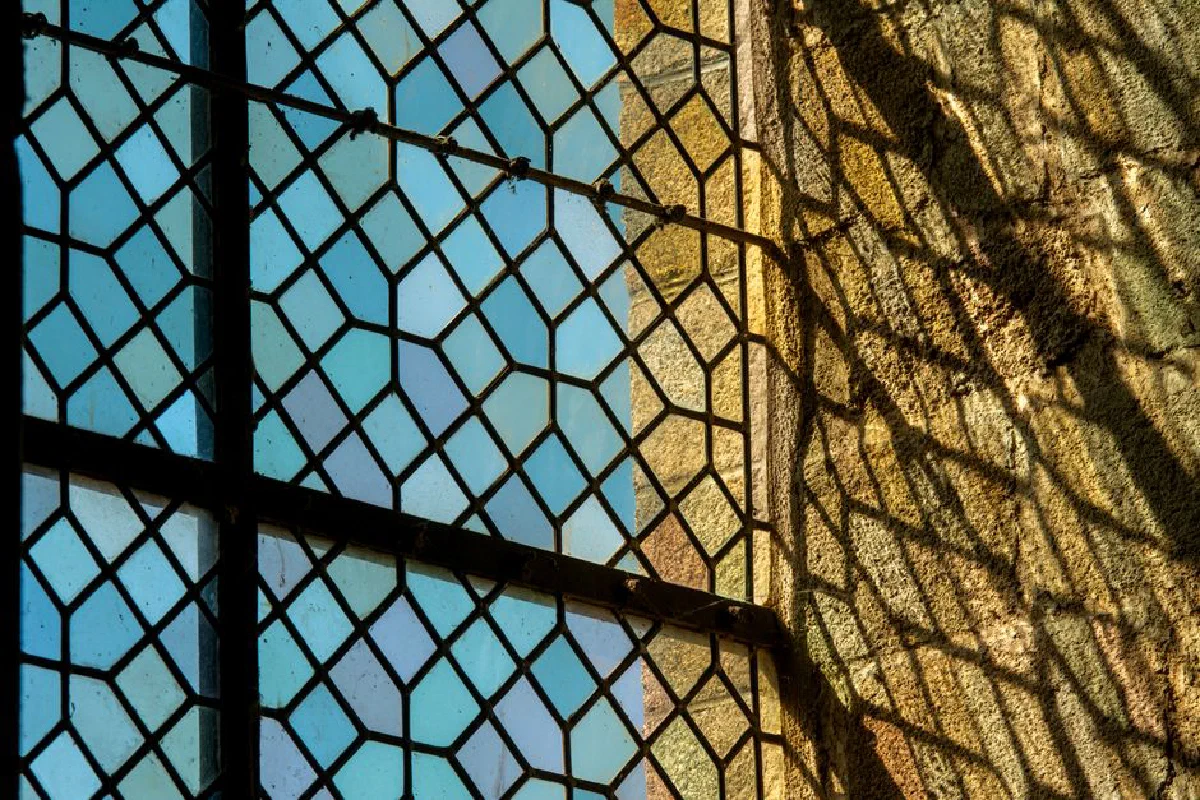 A sunlit stained glass window casting intricate shadows at Le Mont-Saint-Michel, France.