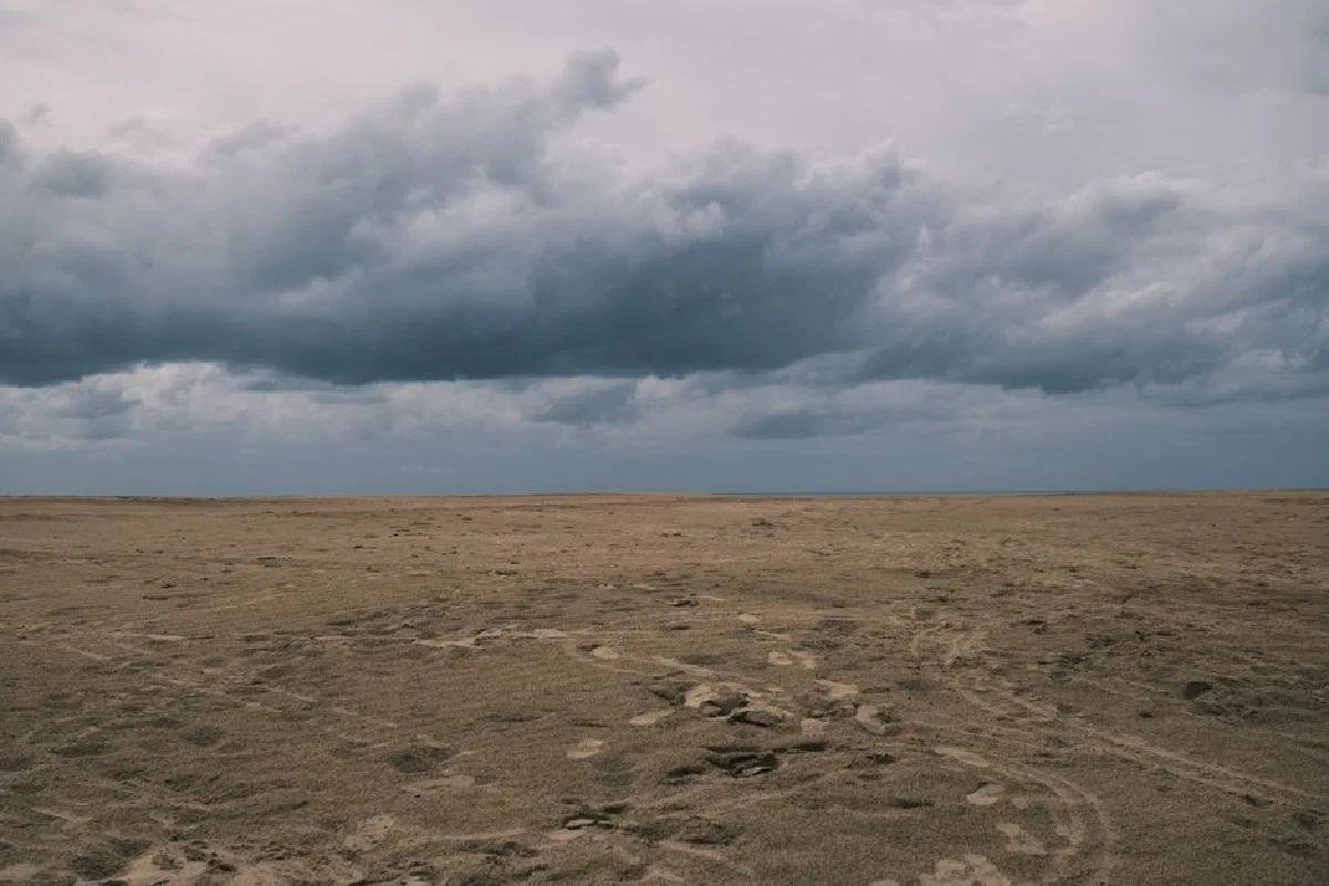 Empty beach with cloudy skies and dramatic clouds, creating a moody atmosphere.