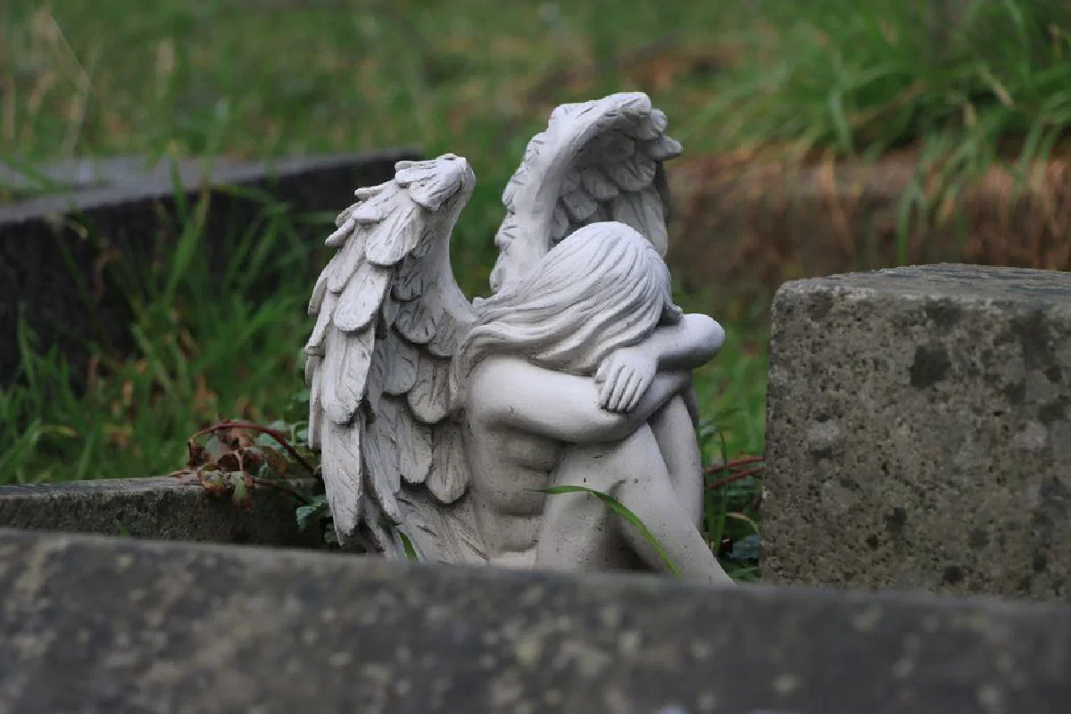 A tranquil angel statue resting in a lush, grassy cemetery conveying peace and serenity.
