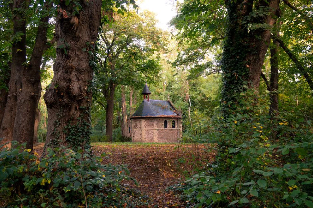 A secluded chapel nestled among lush trees in Sittard, Limburg, during early autumn.