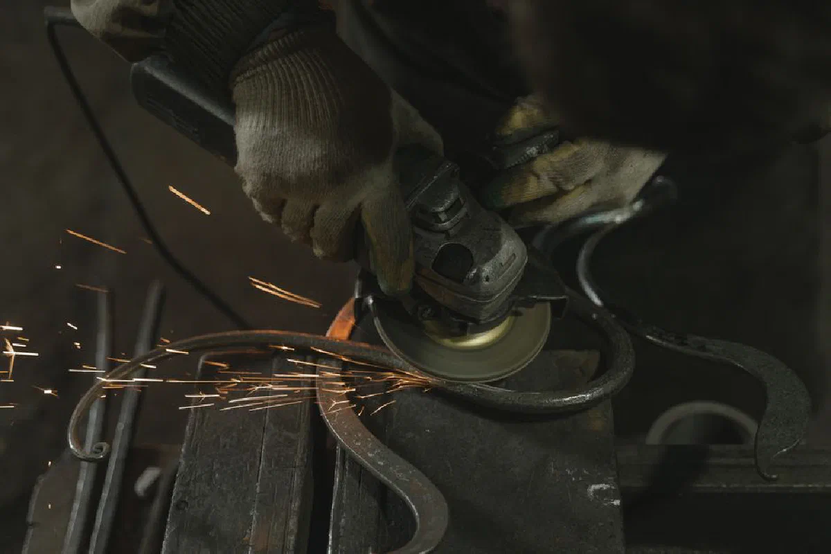 Metalworker using an angle grinder on metal with visible sparks in an industrial setting.