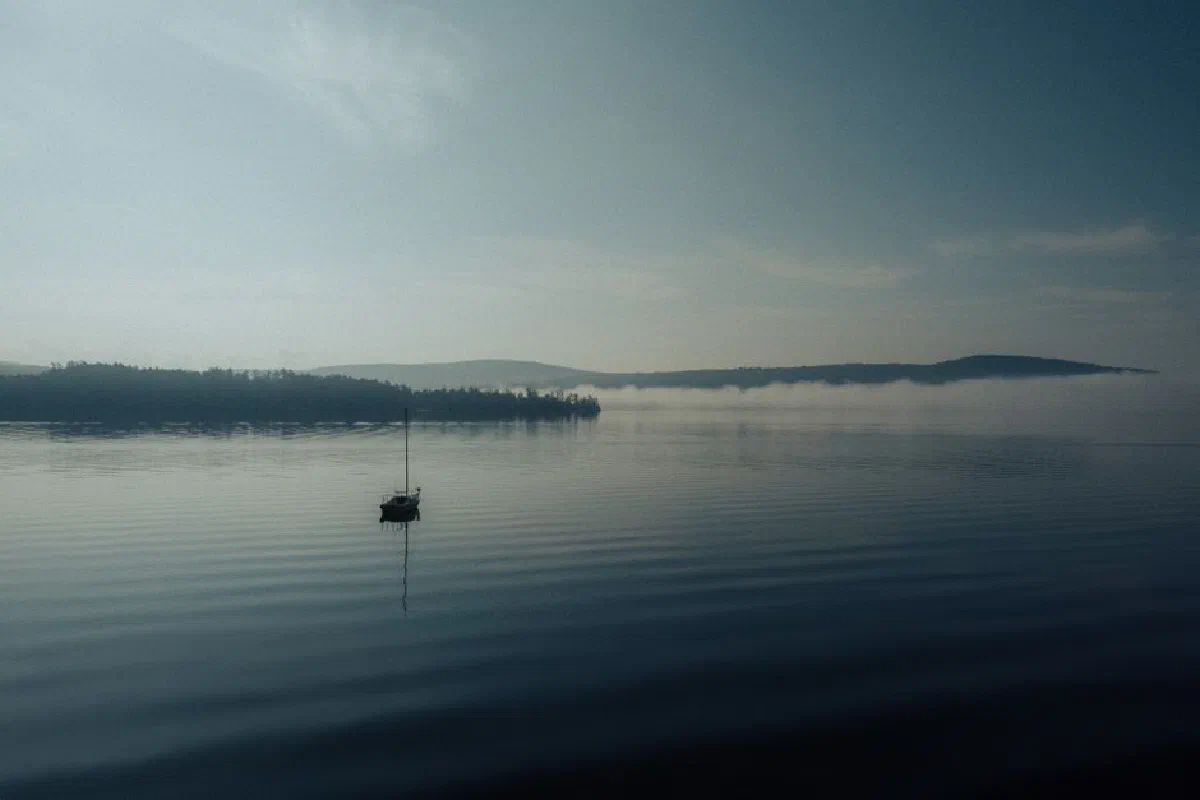 A tranquil scene of a mist-covered lake at dawn with a single boat floating peacefully.