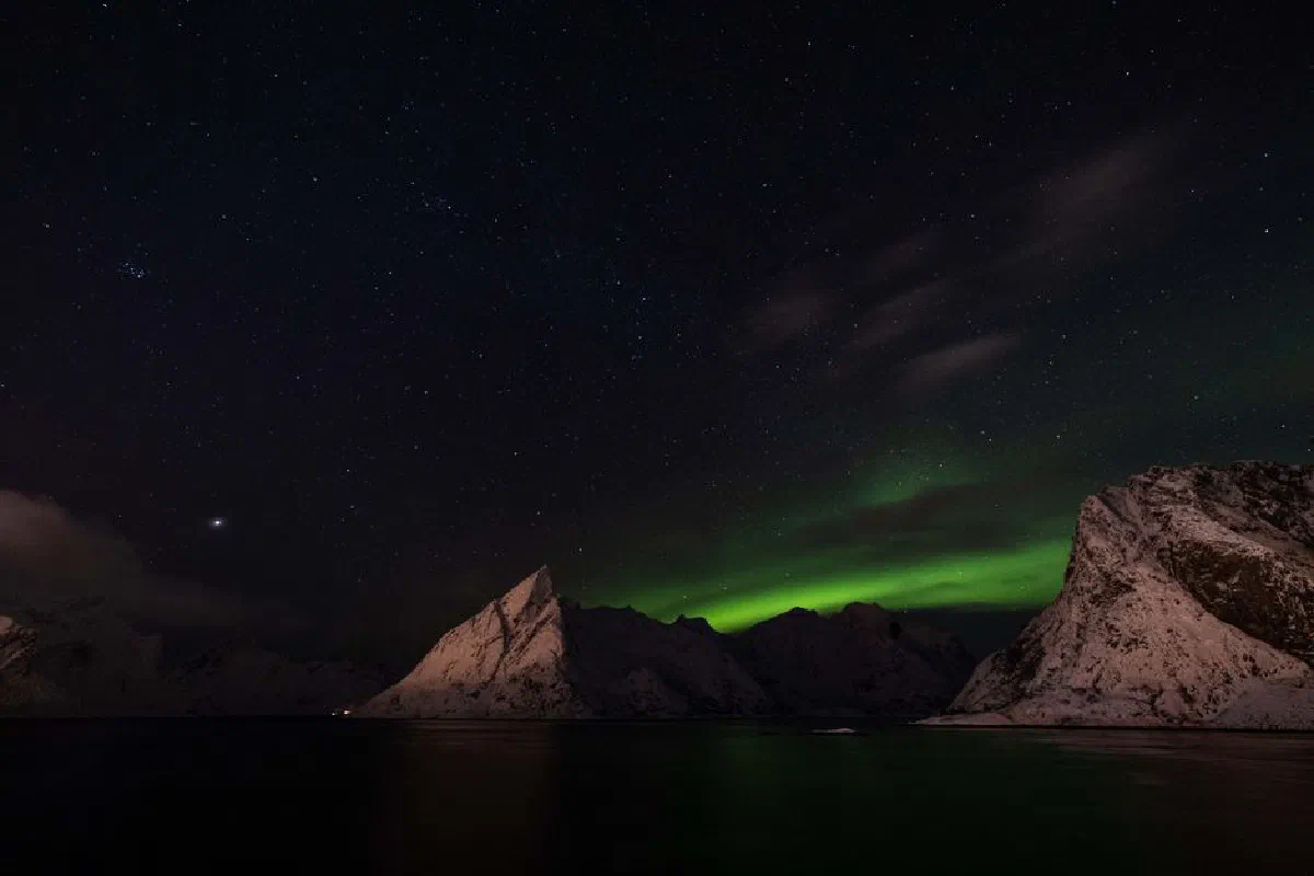 Spectacular view of the Northern Lights illuminating snowy peaks under a starlit sky.