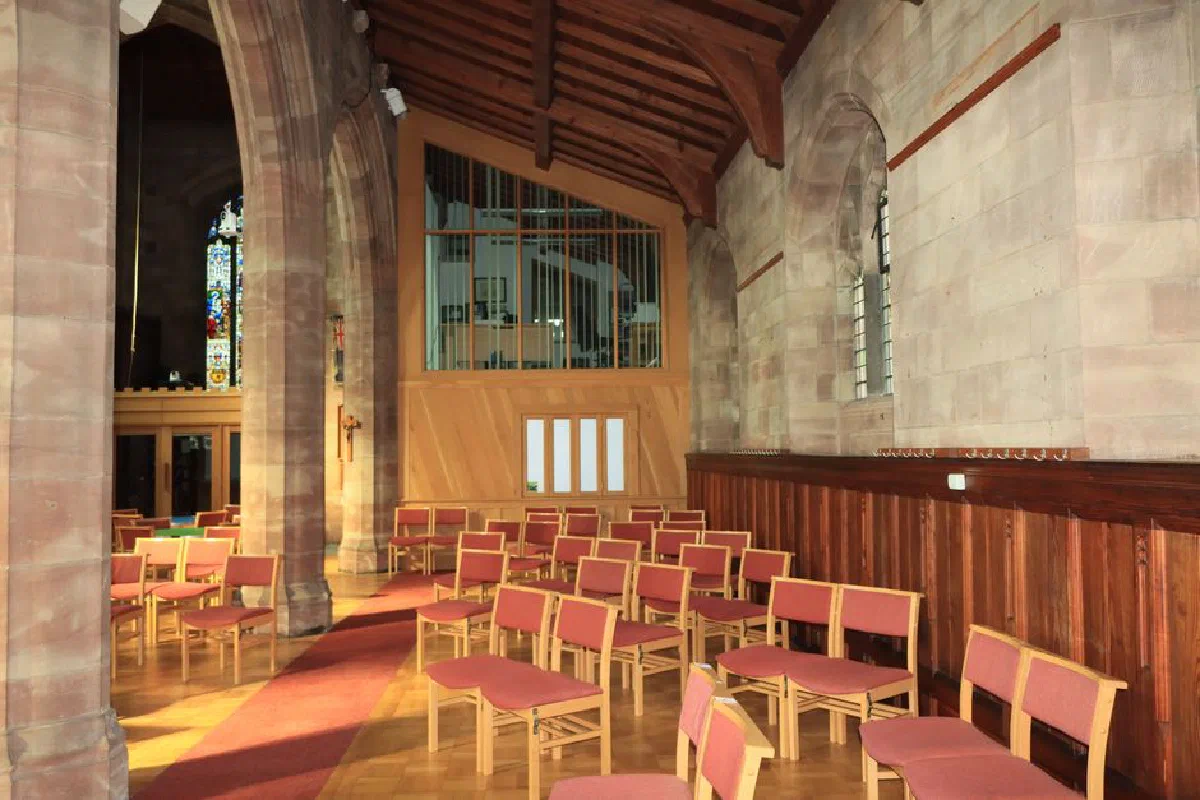 Sunlit seating in a historic church interior with stained glass windows and wooden beams.