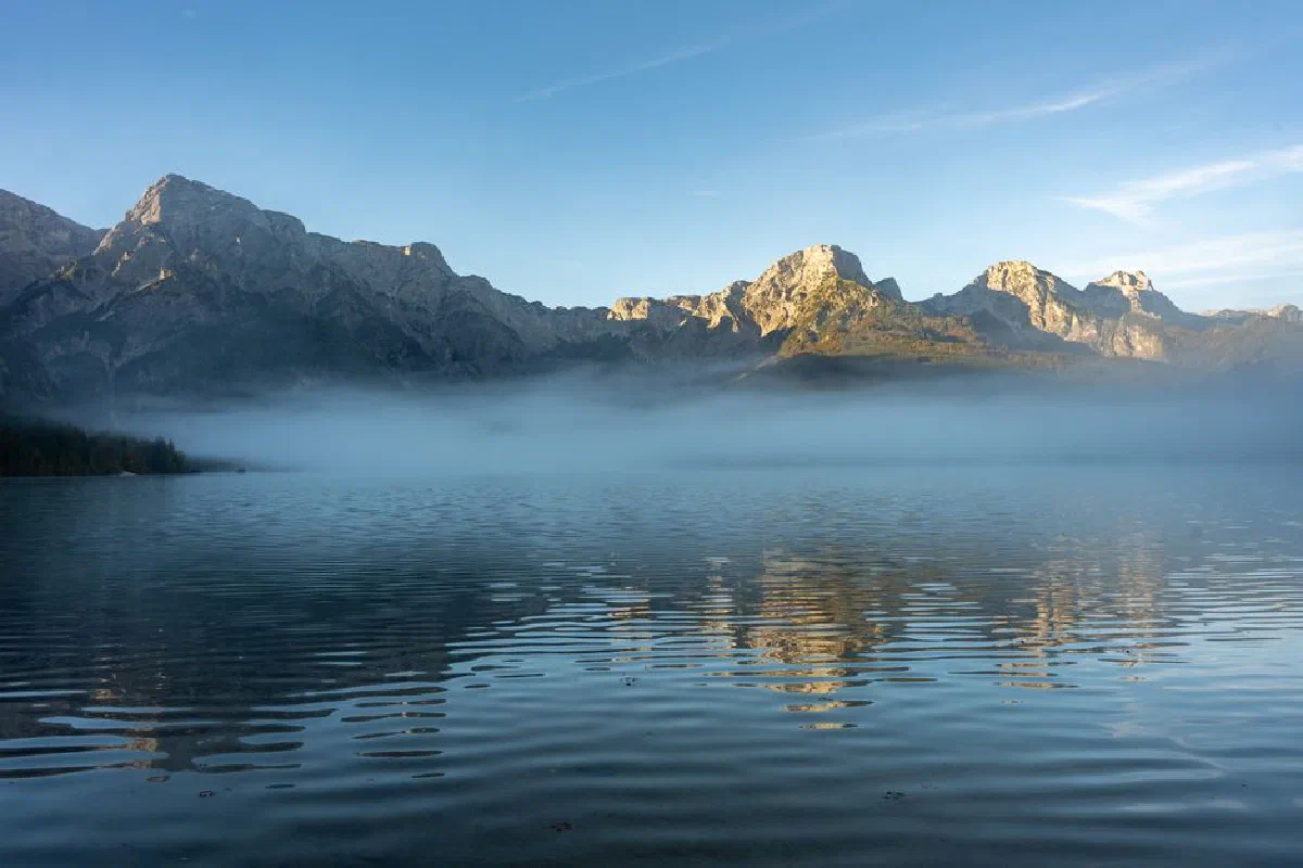 Serene misty lake with reflections of Alpine mountains at sunrise in Oberösterreich, Austria.