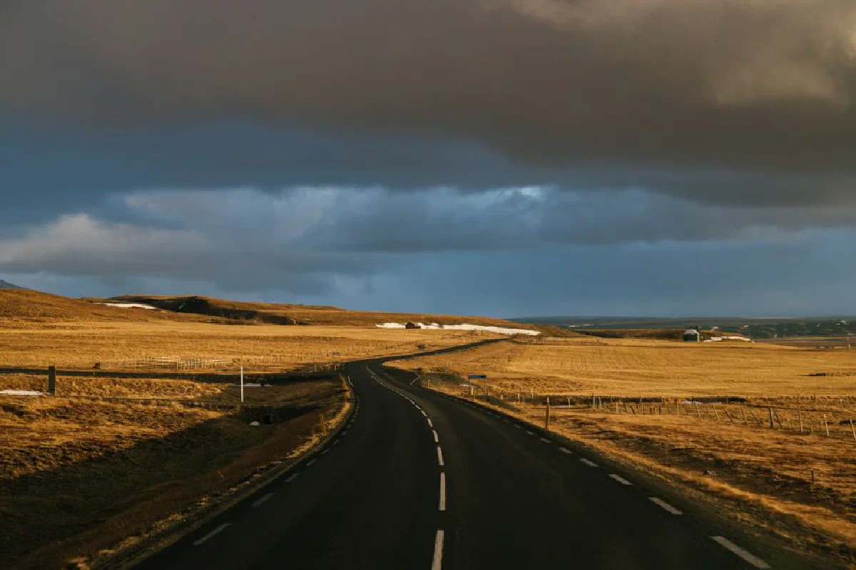 A winding highway through a rural landscape under dramatic autumn clouds, creating an atmospheric scene.