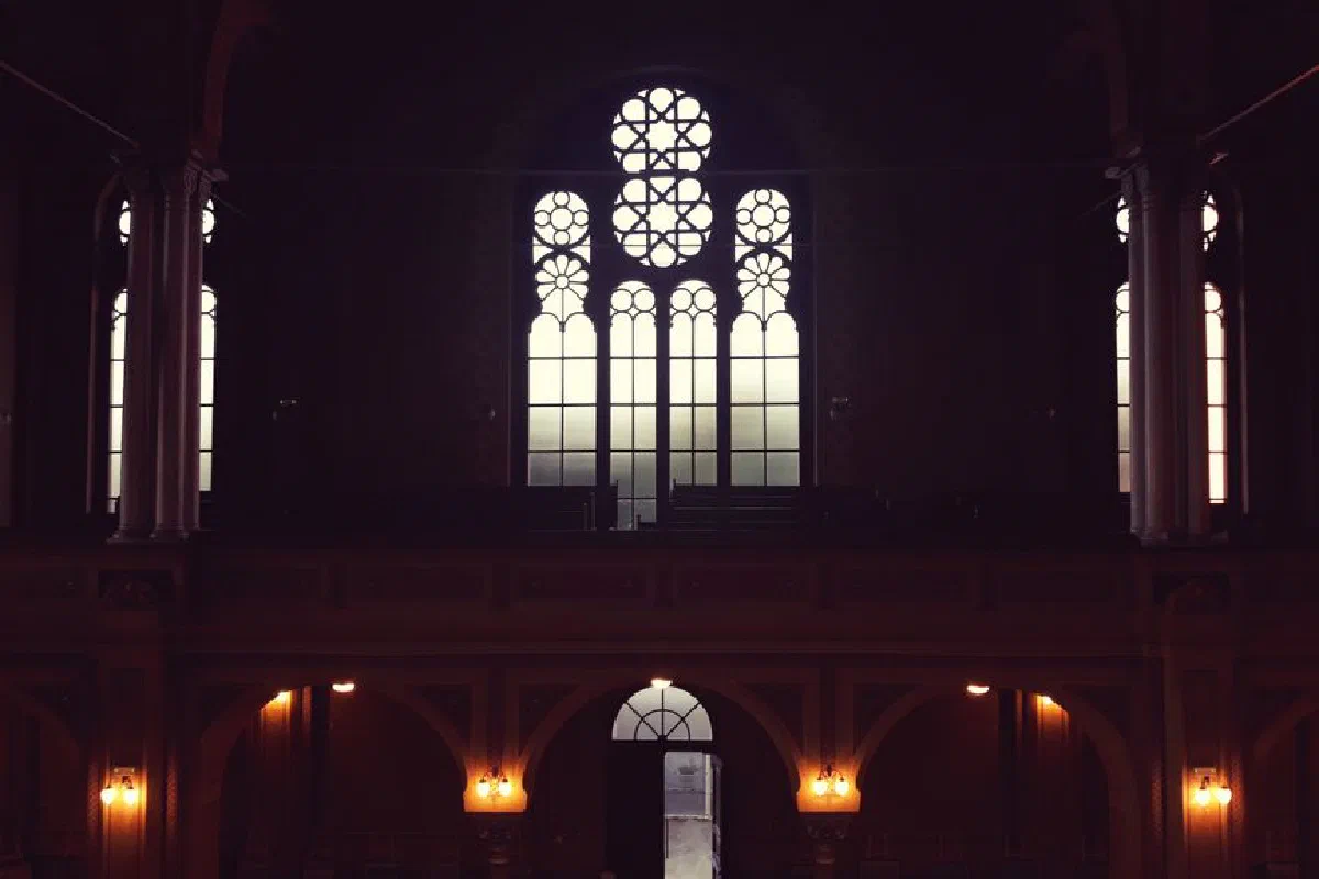 Atmospheric interior of a dimly lit church in Oradea, Romania, highlighting stained glass windows.
