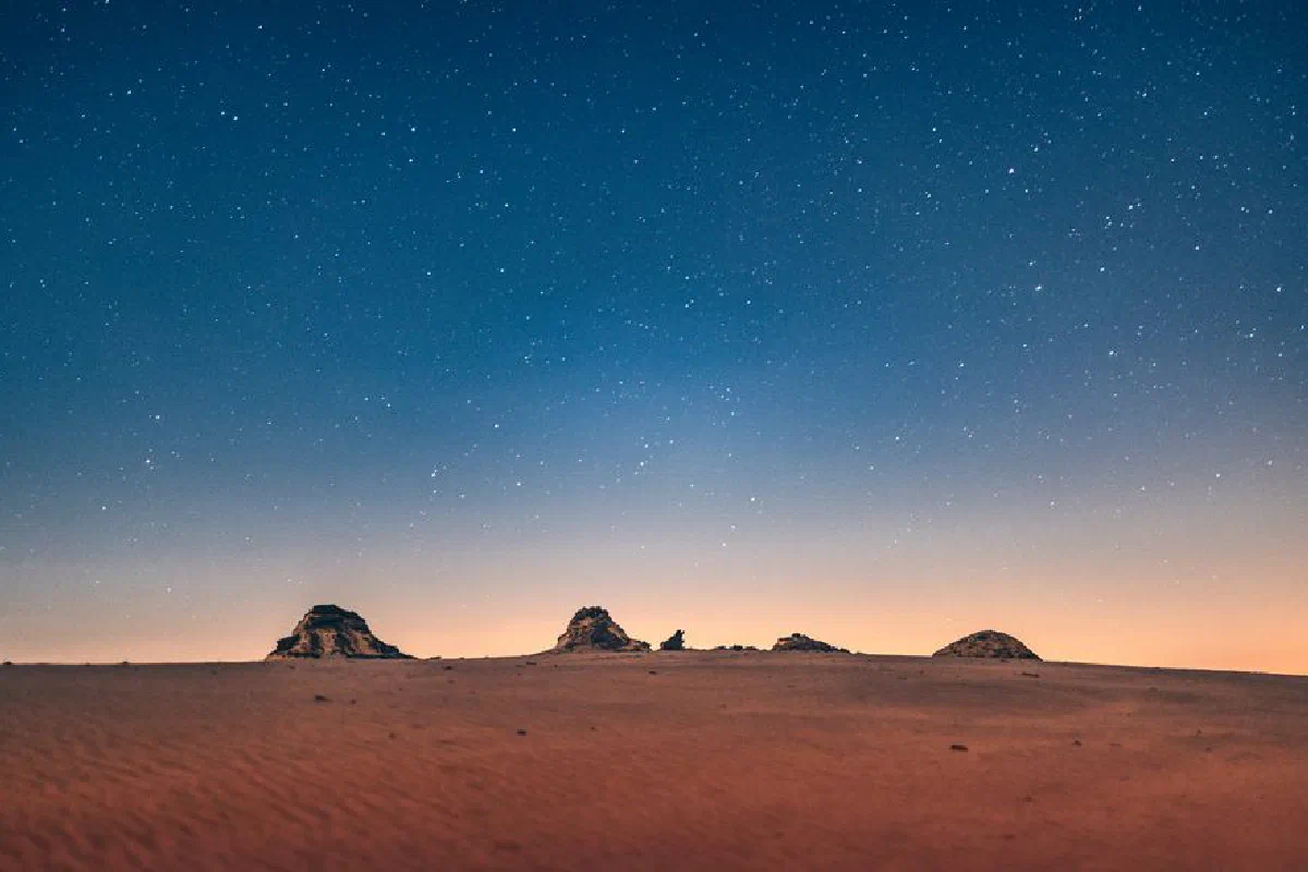 A mesmerizing view of a starry night sky over a tranquil desert landscape.
