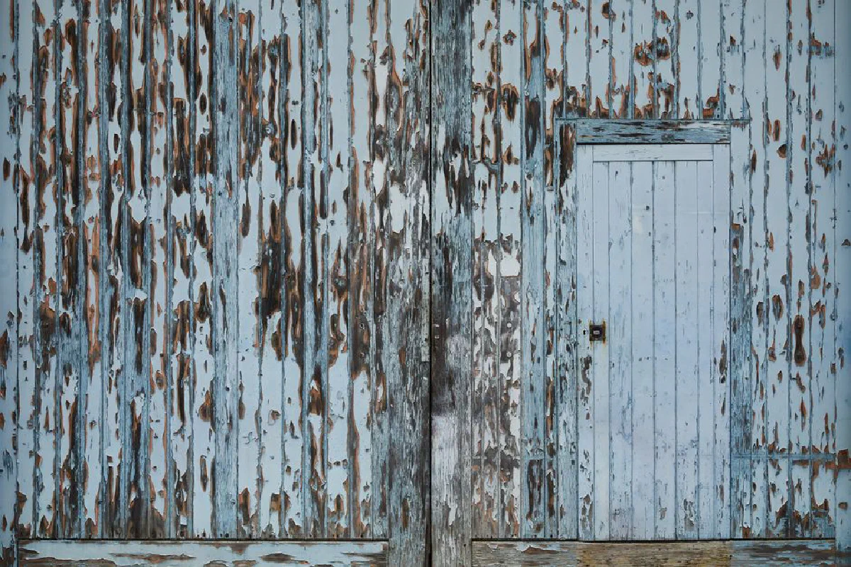 Entrance of aged damaged abandoned wooden warehouse with peeling white paint on wall