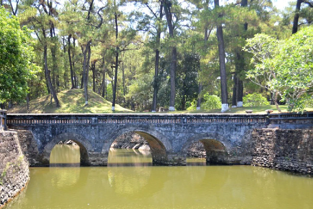Tranquil stone bridge over calm water surrounded by a lush forest, ideal for nature and travel imagery.
