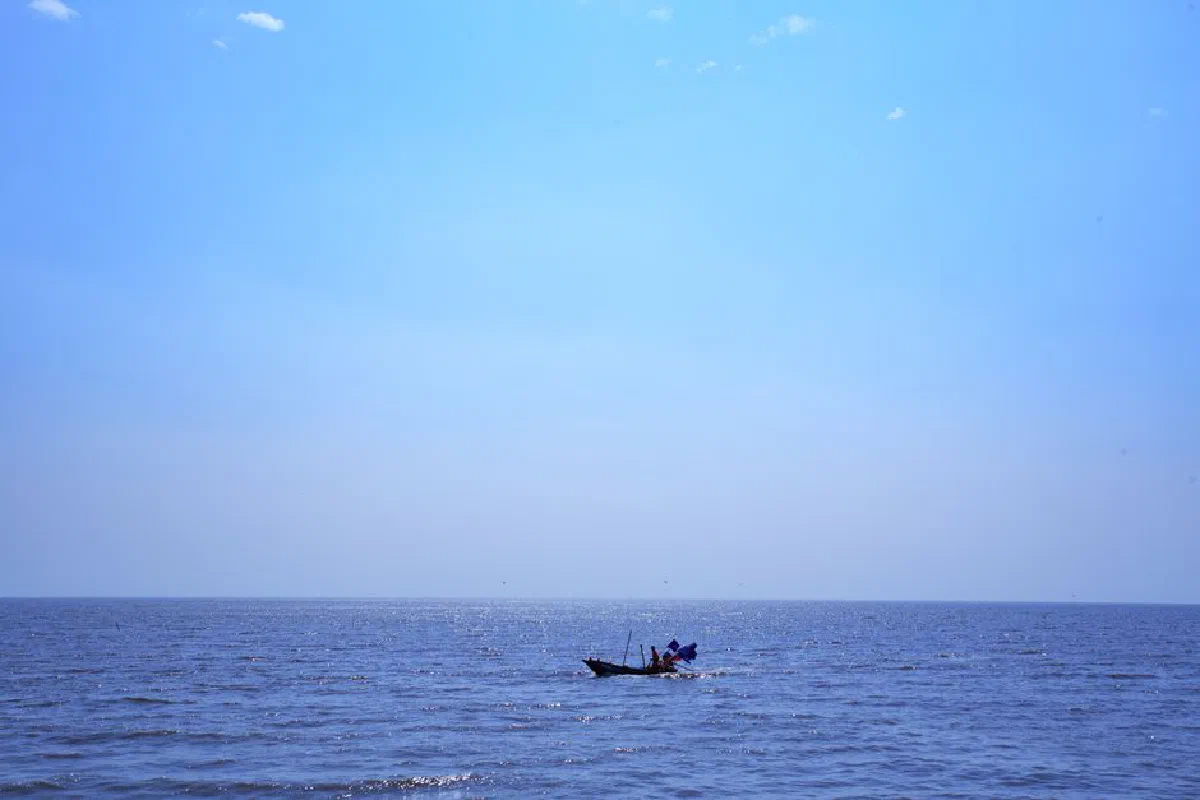 Peaceful ocean scene with a lone fishing boat under a vast blue sky.