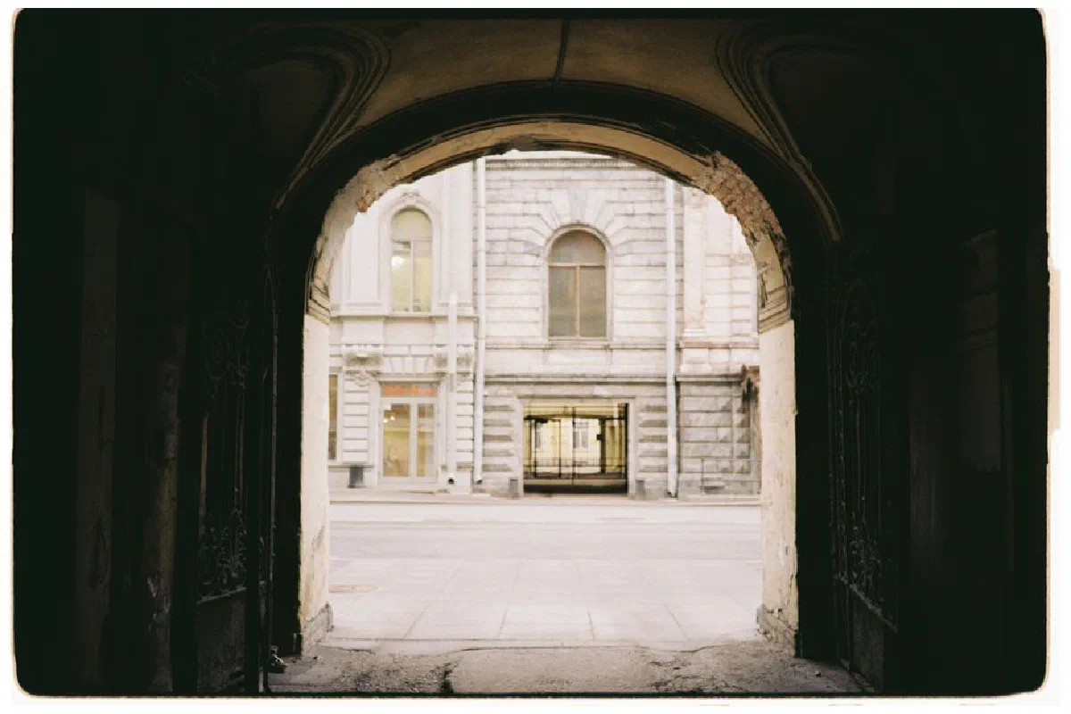 View through a historic stone archway revealing a quiet urban street scene.