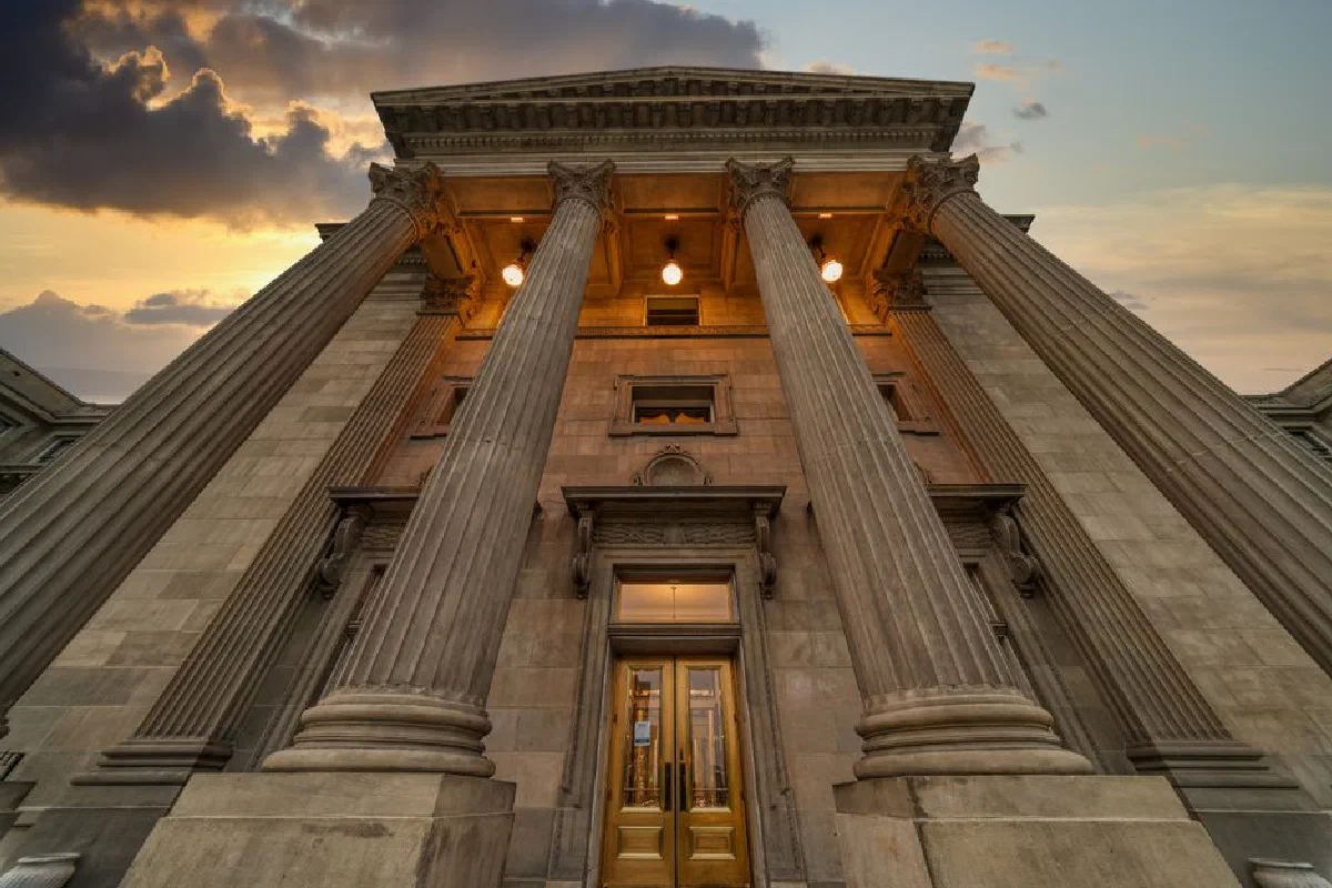 From below of facade of high aged building with colonnade and lamps on ceiling located against sunset sky in evening time in nature