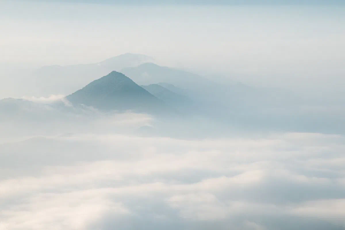 Tranquil mountain peaks emerging through a dense layer of clouds under a clear sky.