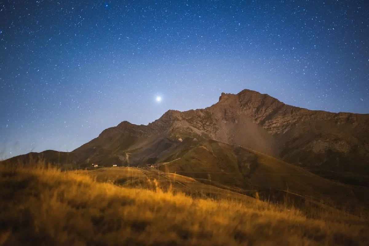 A serene night sky with radiant stars illuminating a picturesque mountain landscape in the Alps.
