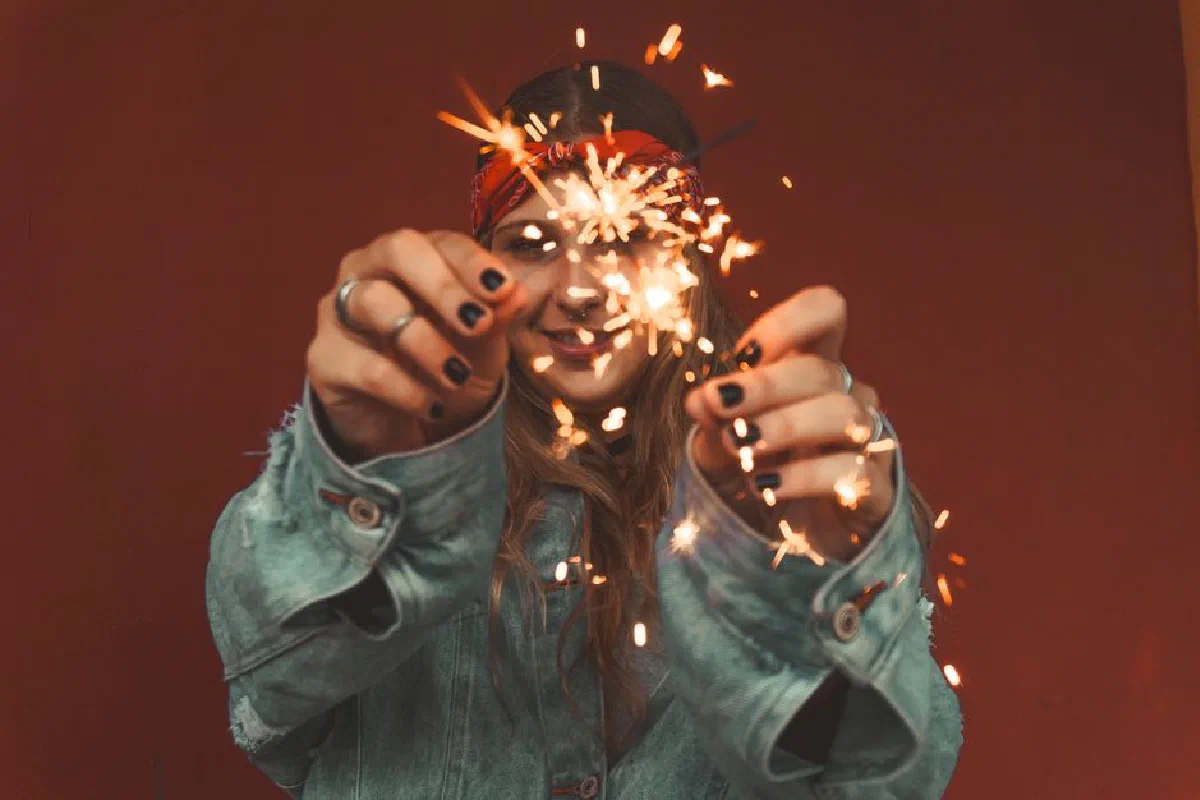 Woman in denim jacket holding a burning sparkler in lively celebration.