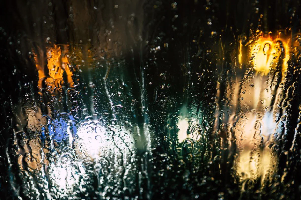 Abstract view of city lights through raindrops on glass, creating a moody and colorful night scene.