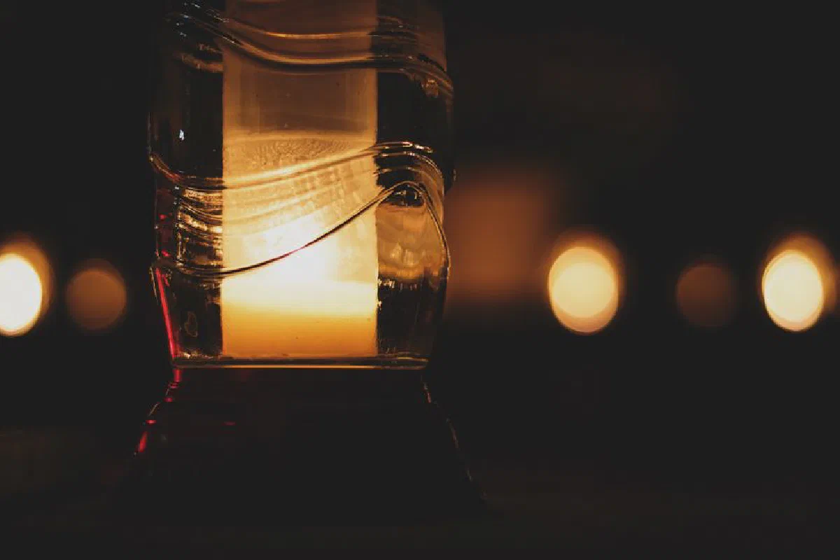Close-up of a glowing candle in glass with bokeh lights creating a cozy atmosphere.