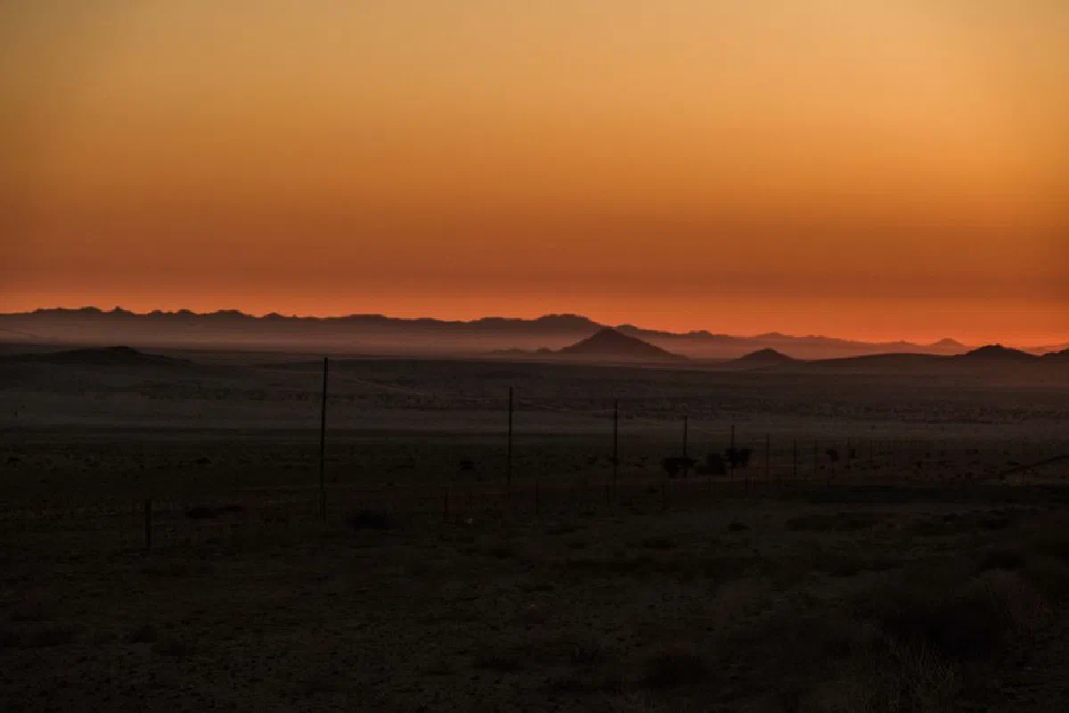 A tranquil sunset over a vast desert landscape with silhouetted mountains and a warm orange sky.