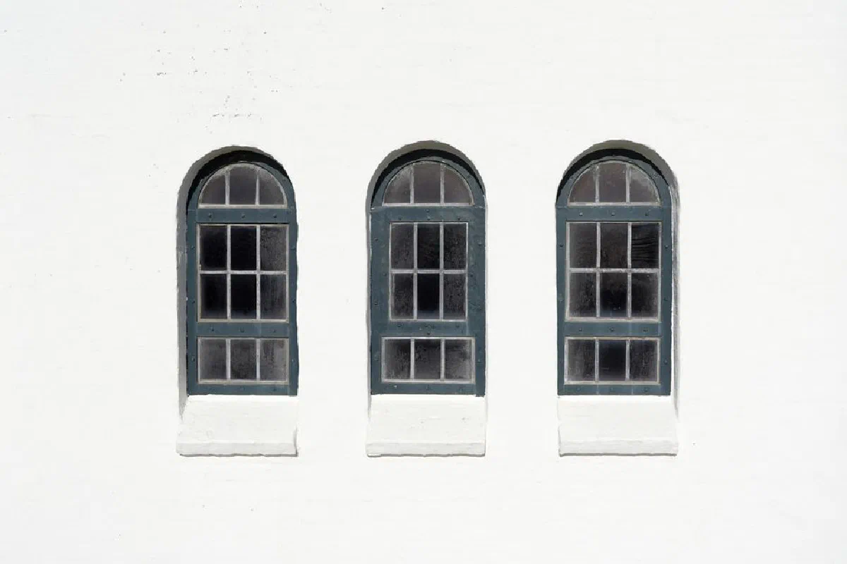 Three arched windows on a white chapel wall in Hvide Sande, Denmark, showcasing symmetry and minimalism.
