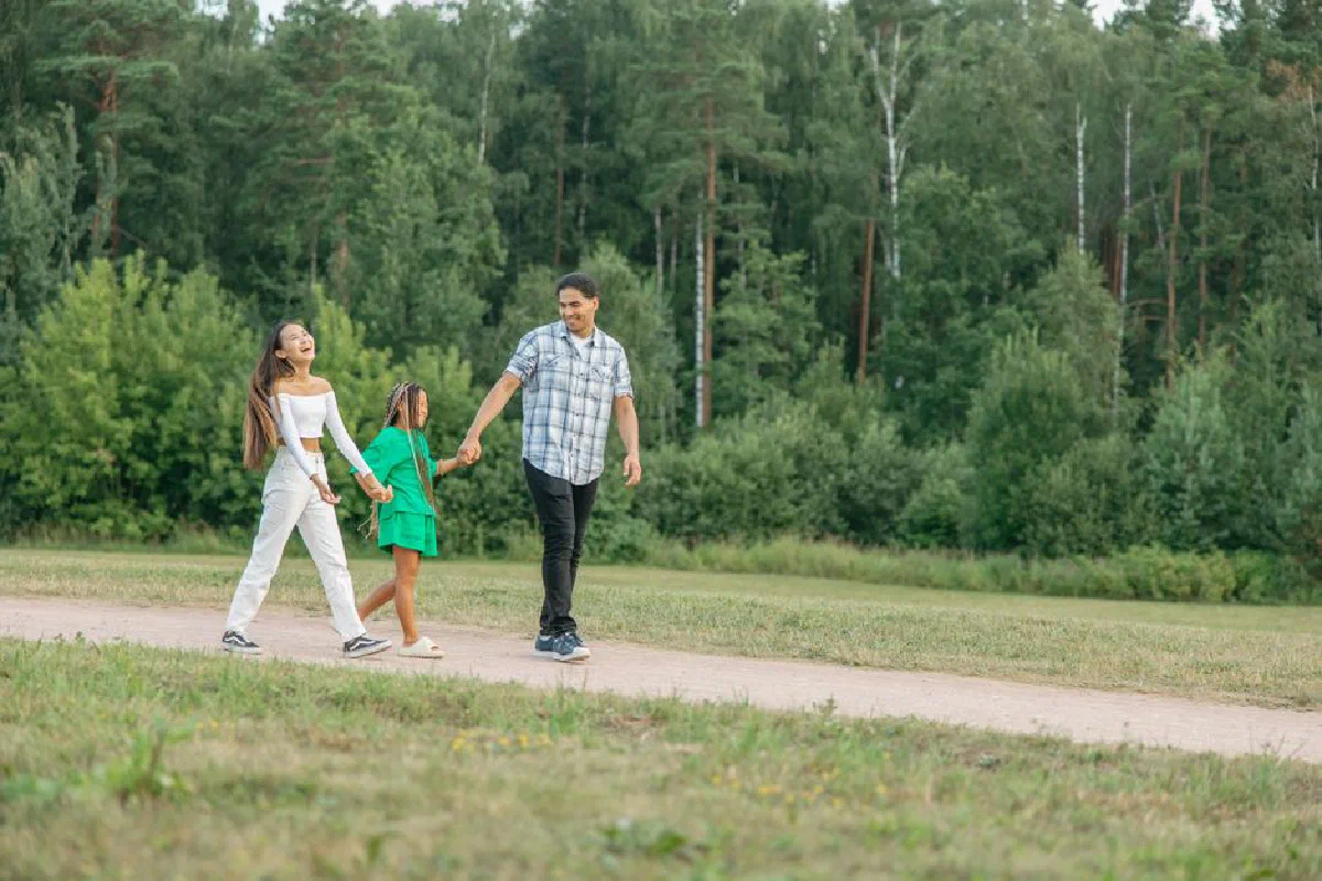A joyful family walking hand-in-hand on a path through a lush green forest park.