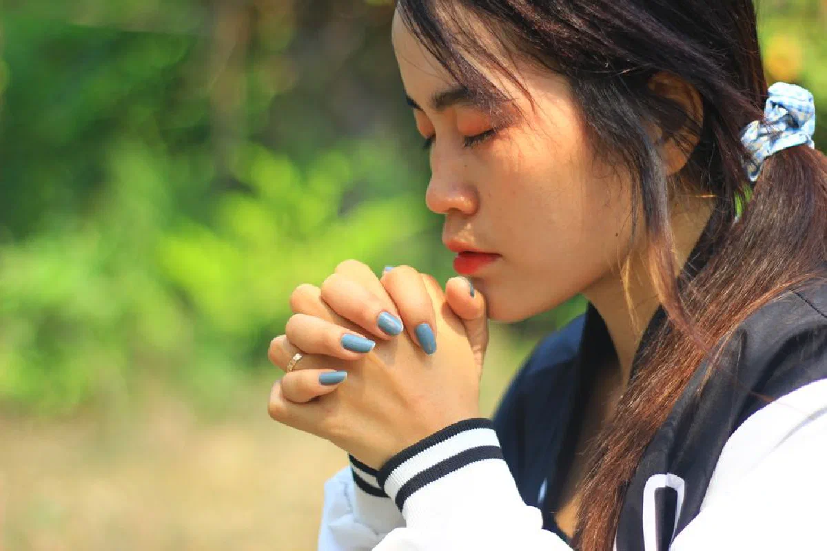Asian woman with closed eyes and hands together in prayer, outdoors in Cambodia.