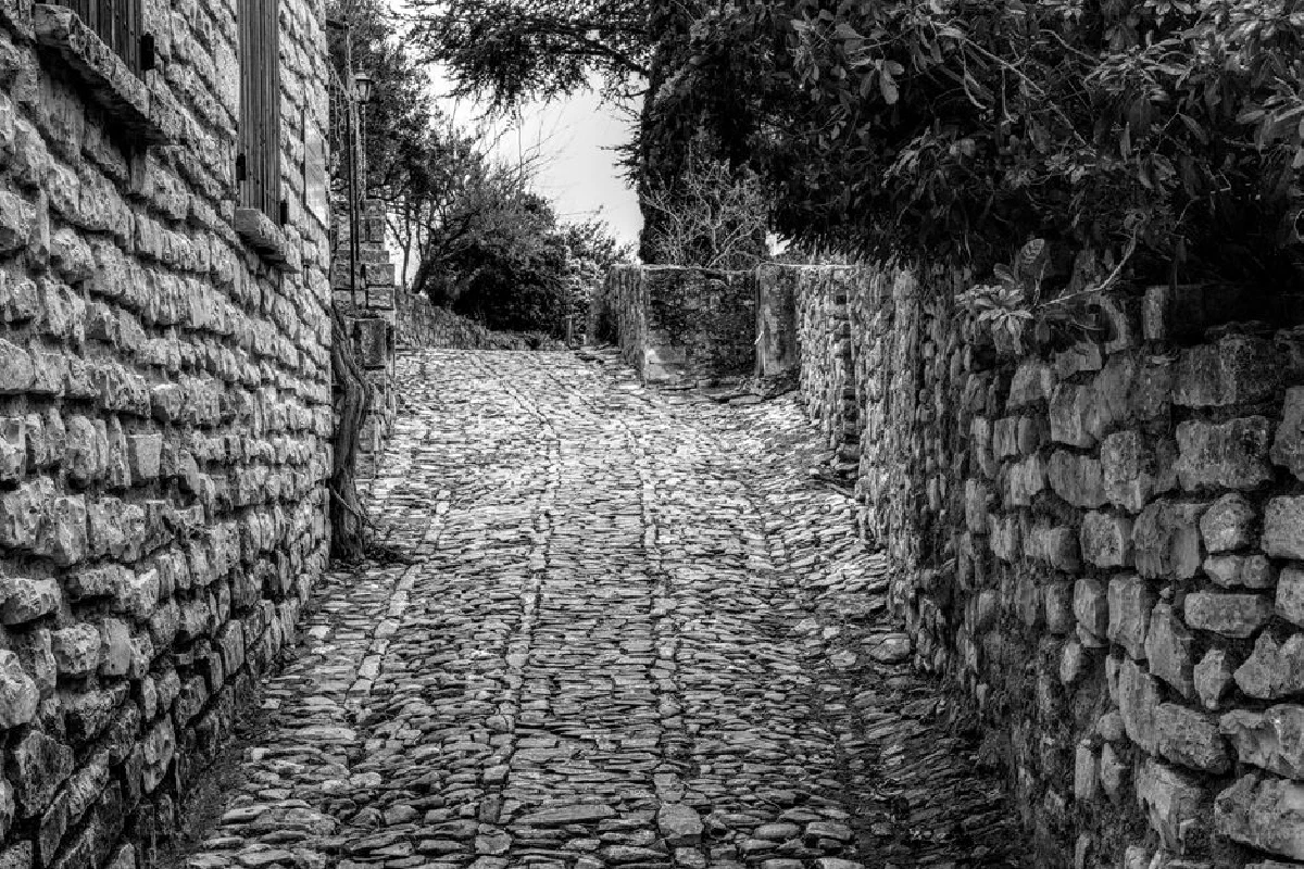 A picturesque cobblestone pathway in a historic French village, surrounded by stone walls.