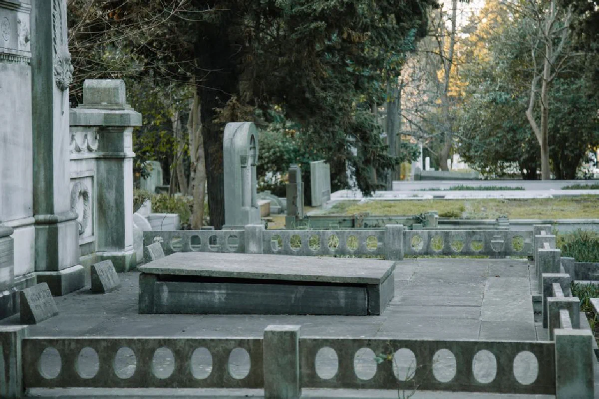 Aged stone graves with sculptures placed in cemetery among green trees in daylight