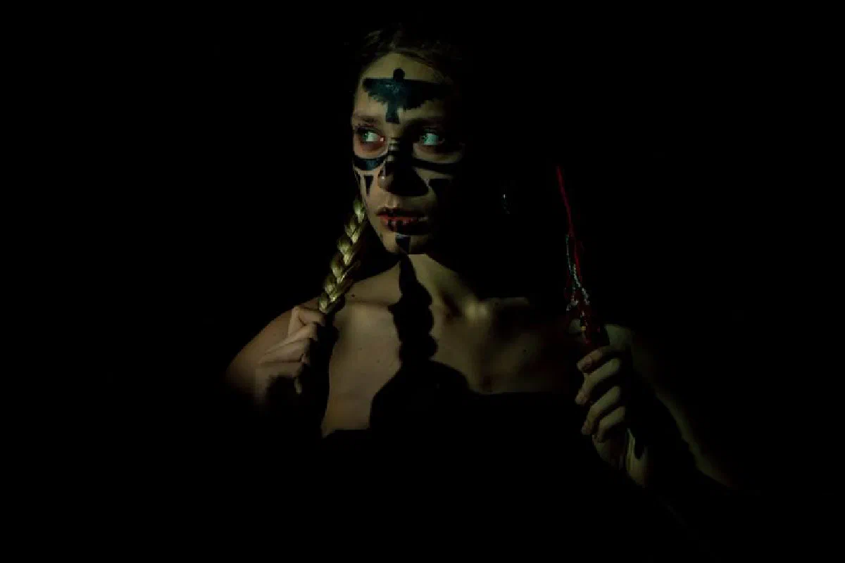 Dark, moody portrait of a woman with braids and warpaint on a black background.