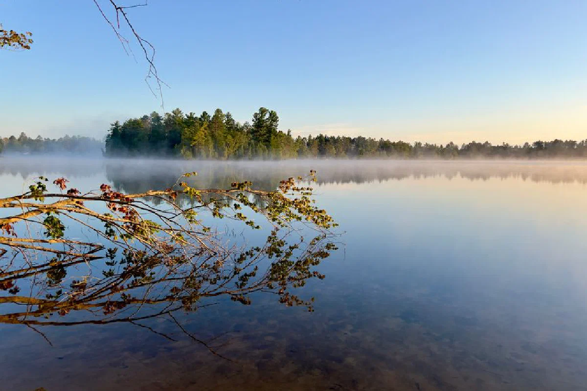 A tranquil lakeside with mist and reflection in Michigan during sunrise.