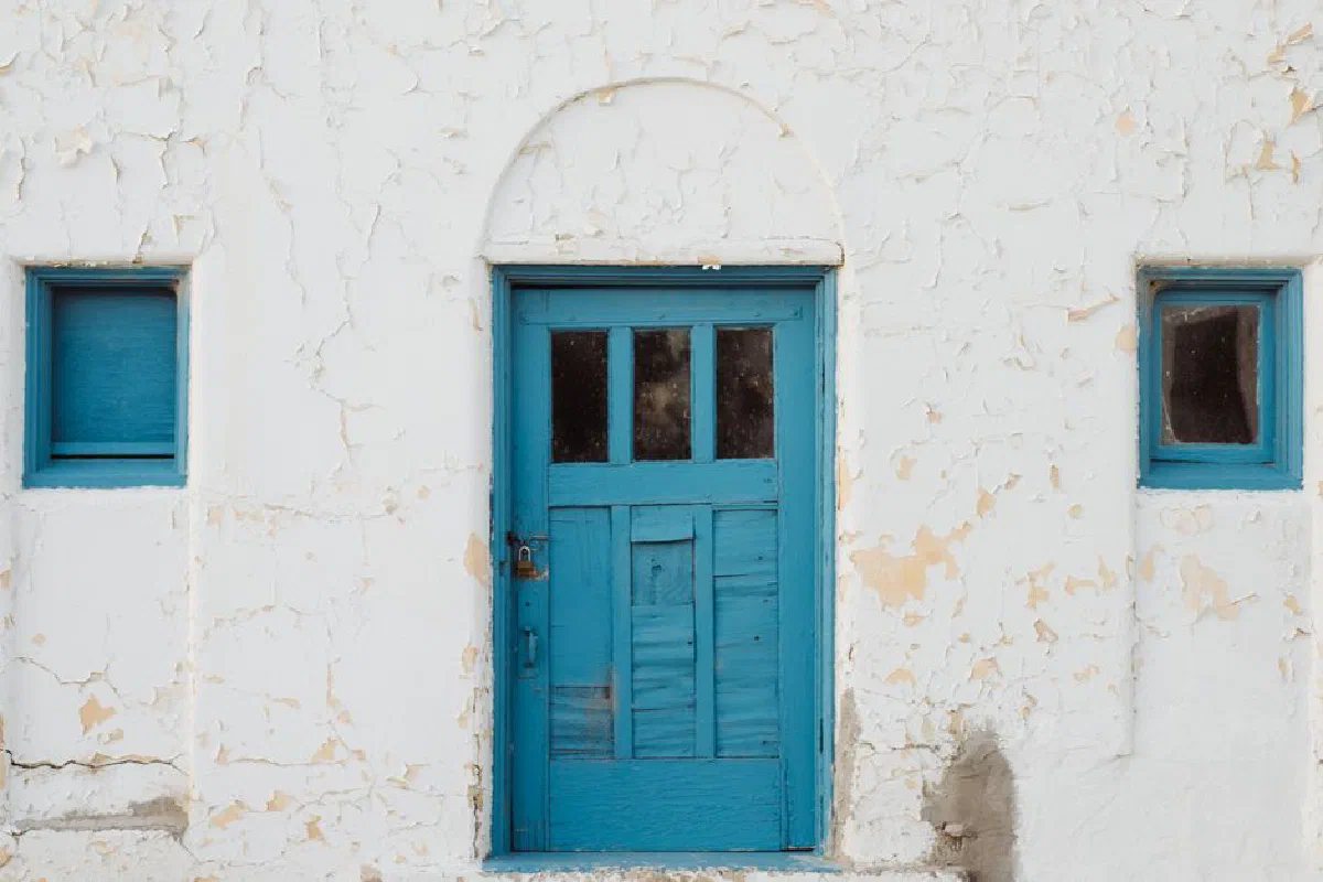 A quaint blue door on a weathered white wall with two blue windows.