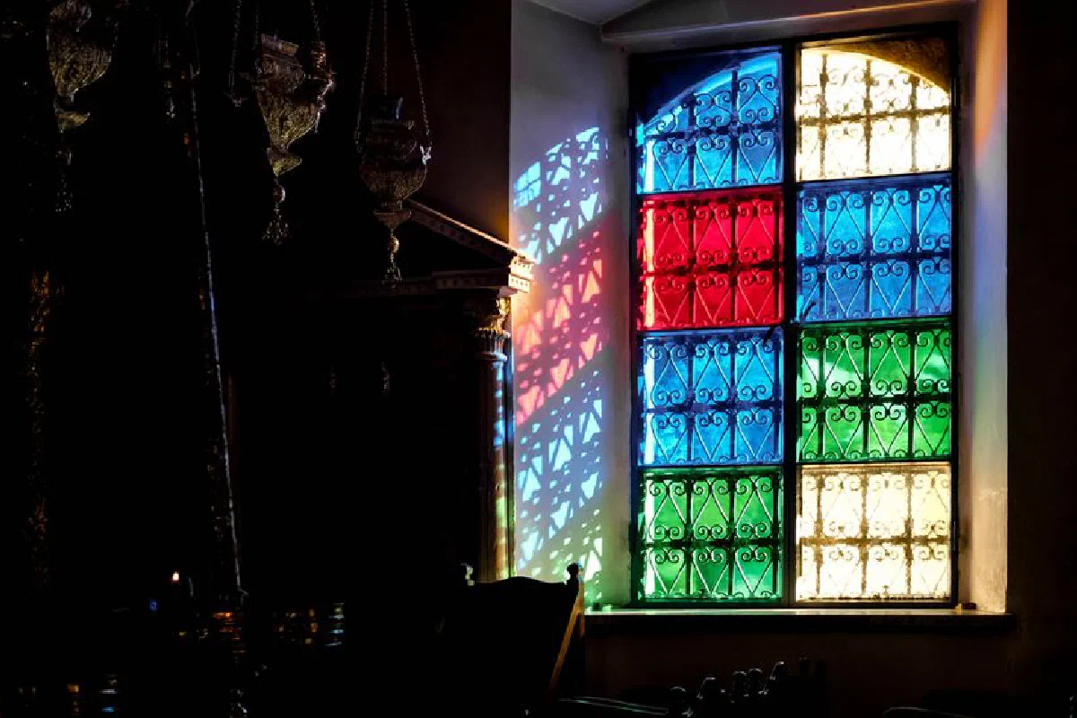 Colorful stained glass window casting vibrant shadows in a dimly lit room.