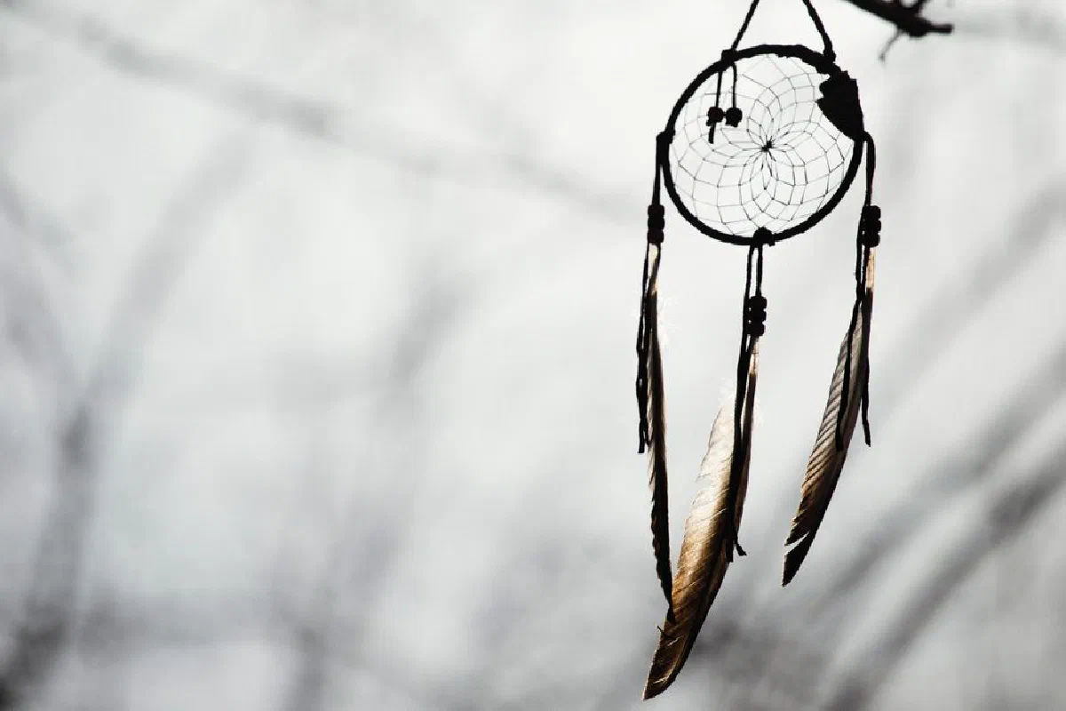 Dreamcatcher hanging outdoors, silhouetted against a soft blurred winter background.