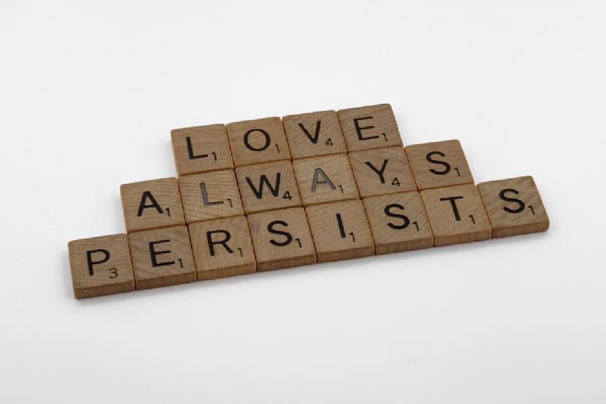 Scrabble tiles on a white background form the phrase 'Love Always Persists', emphasizing a message of enduring love.