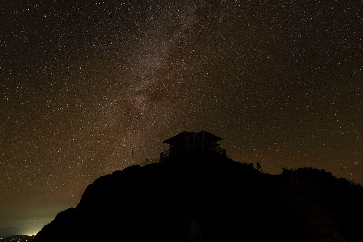 Silhouette of a mountain hut under a starry night sky, showcasing the Milky Way.