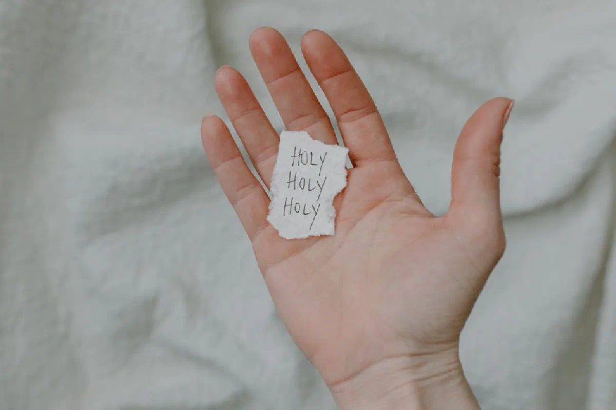 A close-up of a hand holding a paper with 'Holy' written, showing a spiritual theme.