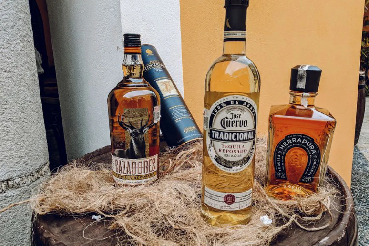 A collection of tequila bottles arranged outdoors on a rustic barrel.