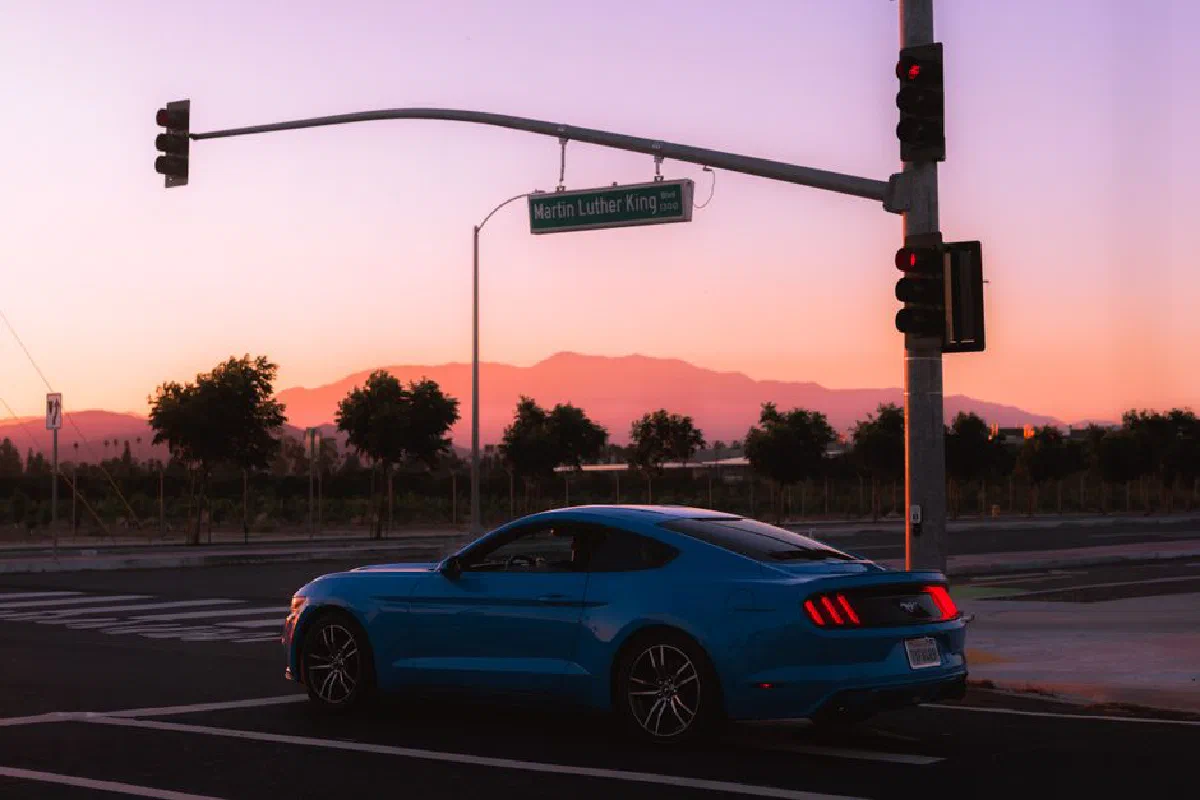 Blue sports car at a road intersection during sunset with a mountainous backdrop.