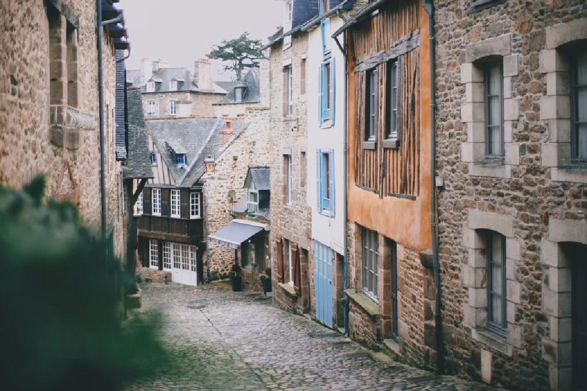 Narrow cobblestone street with attached old brick and stone buildings in historic town on cloudy day