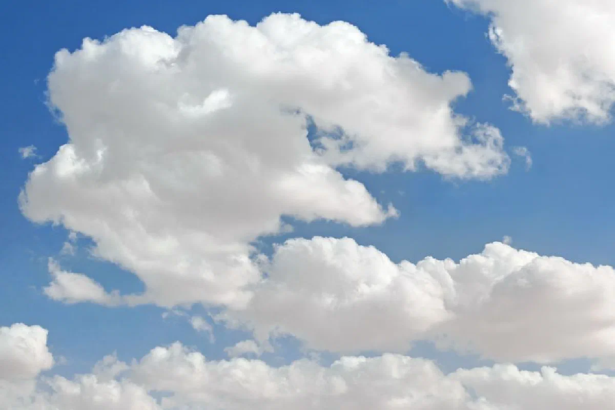 A landscape of fluffy white clouds scattered across a pristine blue sky.