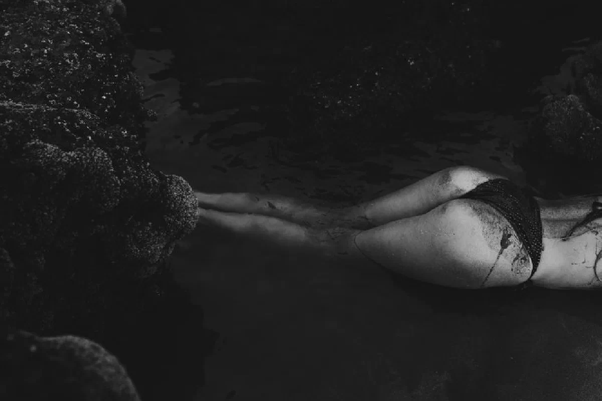 Black and white photo of a serene beach scene with rocks and a person lying in water.